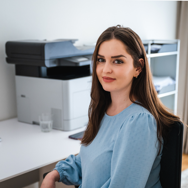 Eine Frau sitzt an einem Schreibtisch vor einem Drucker.